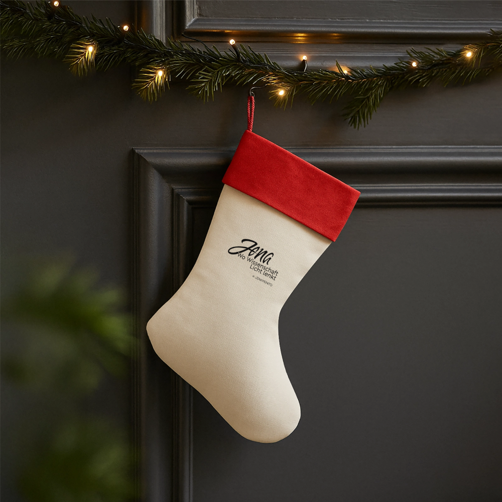 Weihnachtsstrumpf im Jena.Lichtschrift-Design an dunkler Wand mit Tannengrün und Lichterkette